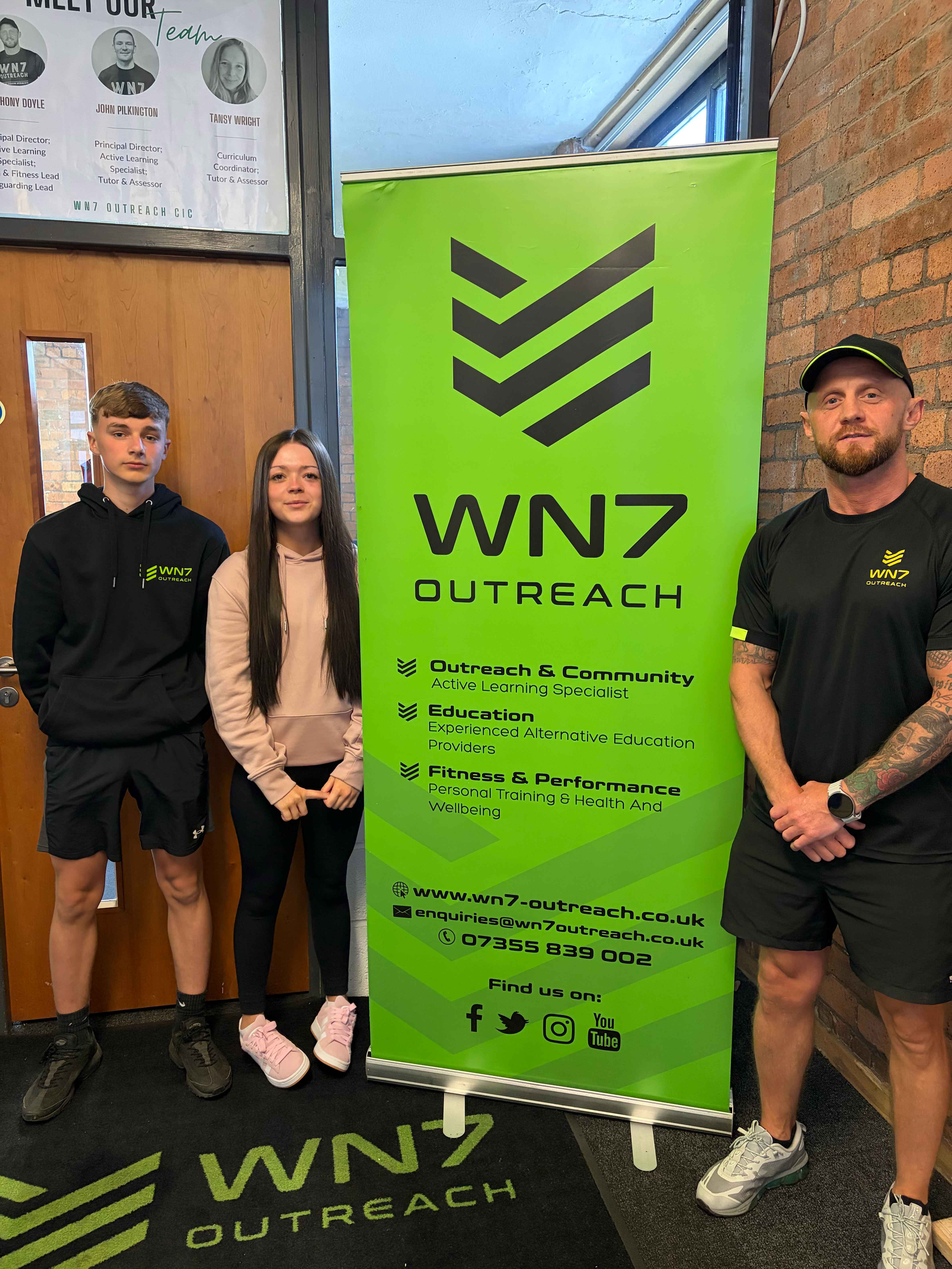 Three people with a WN7 outreach pull-up banner Three people with a WN7 outreach pull-up banner